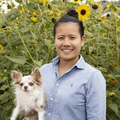 Chiropractor American Fork UT Debbie Pun Meet The Team with dog Platinum Chiropractic Chiropractor, Debbie Pun, smiling in sunflower field holding dog.